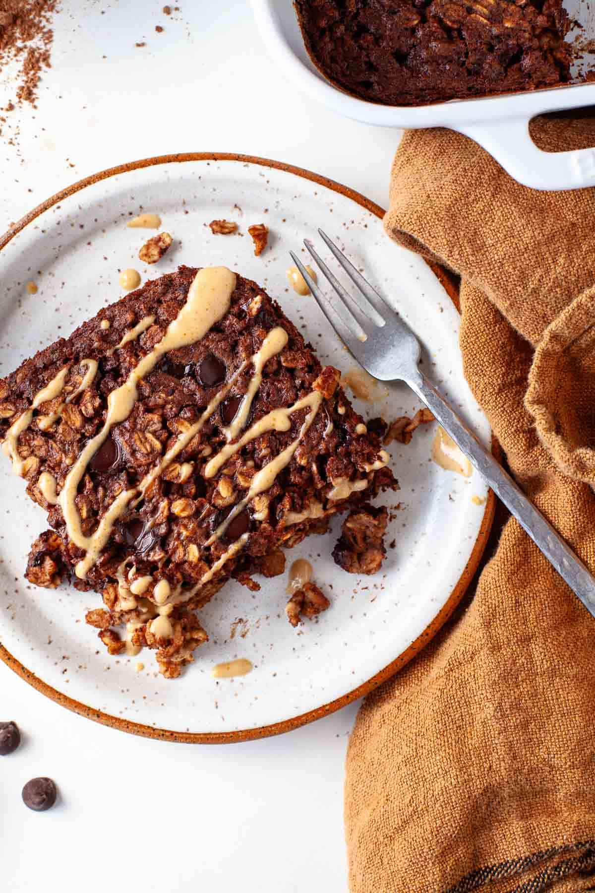 chocolate baked oatmeal drizzled with peanut butter on white speckled plate.