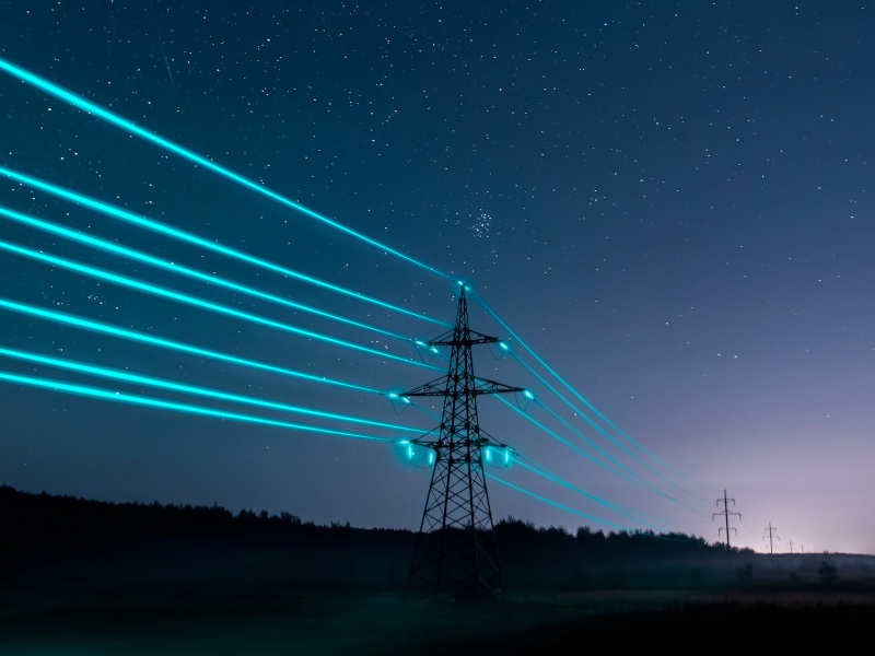 An electricity tower sits against a dark, dusky sky with blue glowing power lines stretching off into the distance.