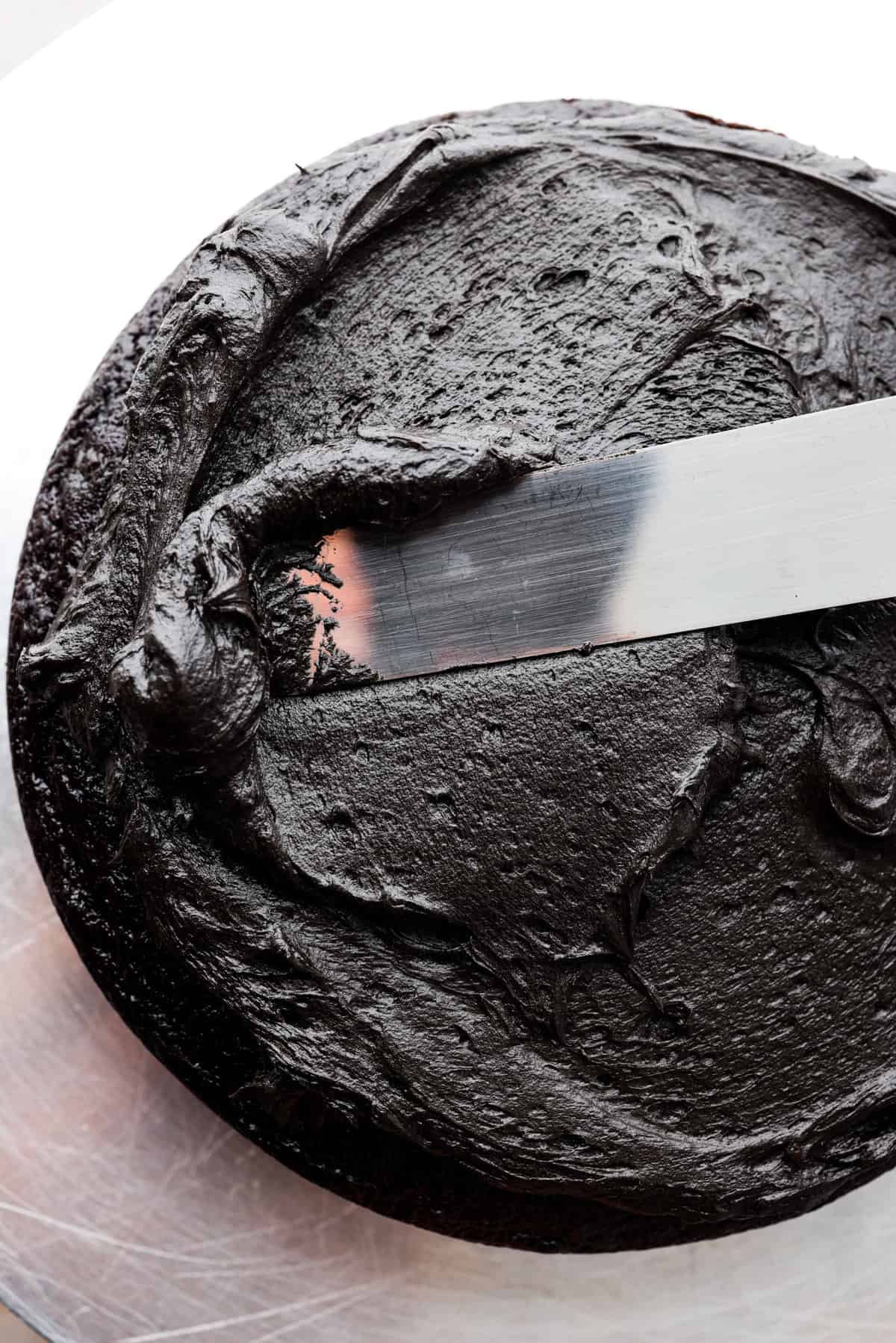 Overhead shot of someone frosting a cake with black frosting.