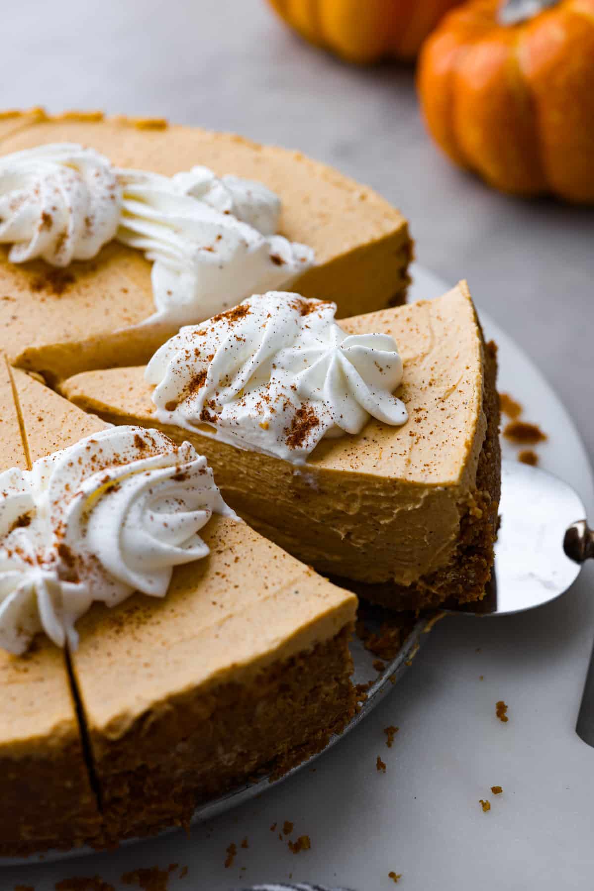 Angle shot of someone taking a slice of the no-bake pumpkin cheesecake with whipped cream on top.