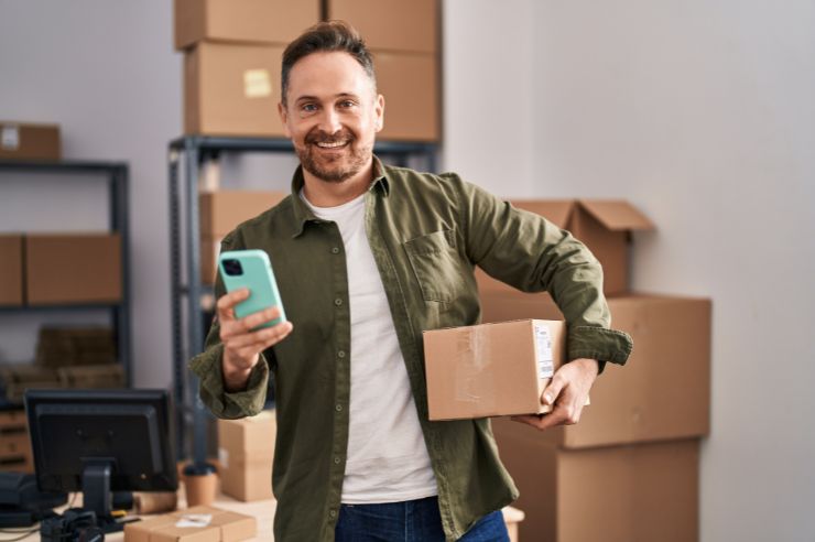 Happy man with smartphone and shipping boxes.