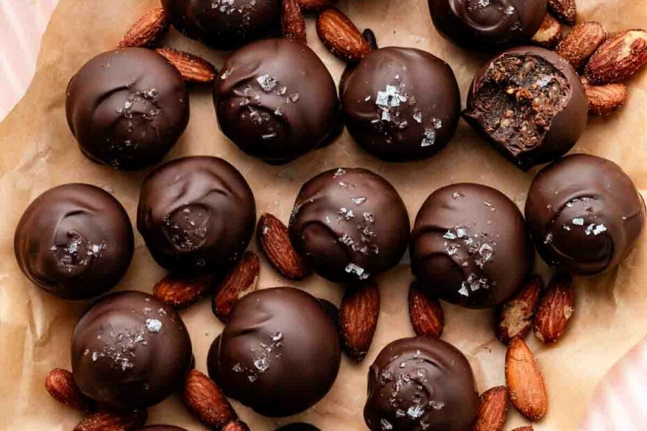 healthy date almond truffles coated in chocolate and sea salt placed with almonds on a pink plate.