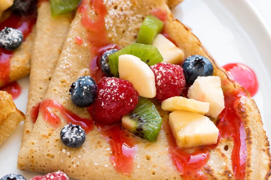 Close up photo of healthy oat crepes with chopped fruit and berry syrup.
