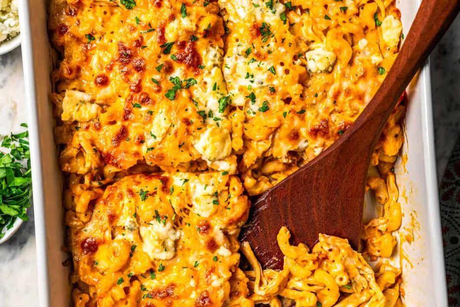 Overhead view of a wooden serving spoon resting in an open serving of buffalo mac and cheese in a casserole dish.