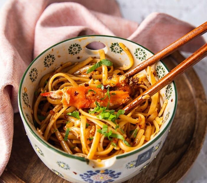 two chopsticks over a bowl of creamy chili crab pasta with a large chunk of cooked crab over the chili tossed pasta