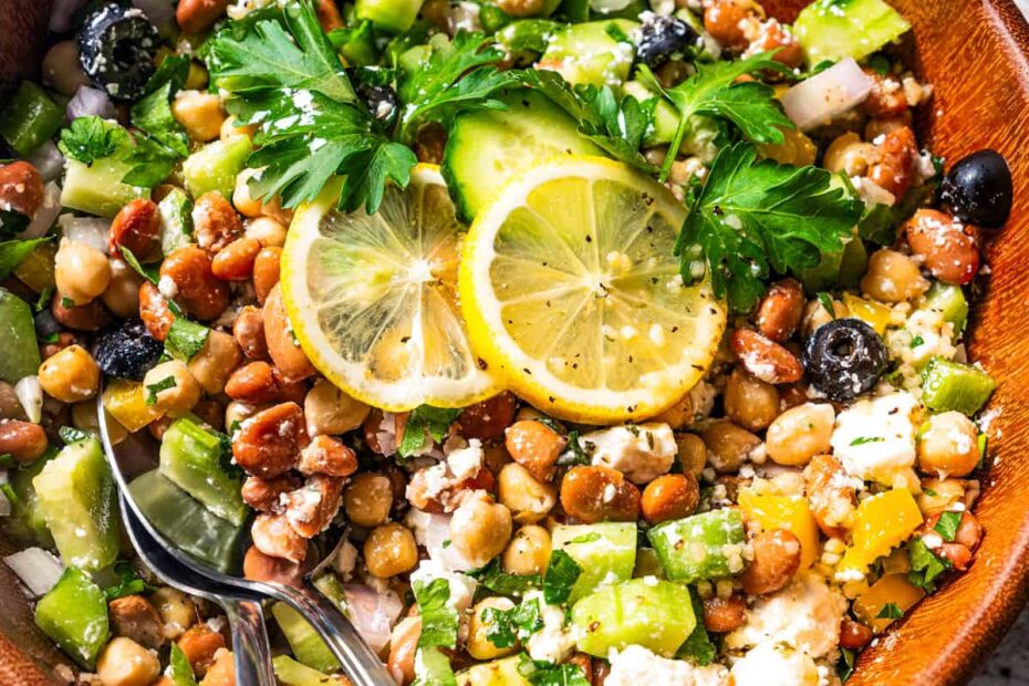 Dense bean salad in a wooden bowl with a pair of salad tongs.