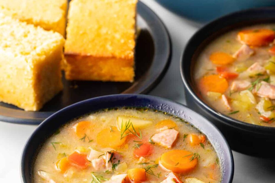 Two black bowls of ham and cabbage soup next to a black plate with 3 squares of cornbread.
