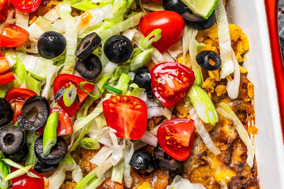 Close-up shot of a taco casserole in a baking dish garnished with olives, tomatoes, and shredded lettuce.