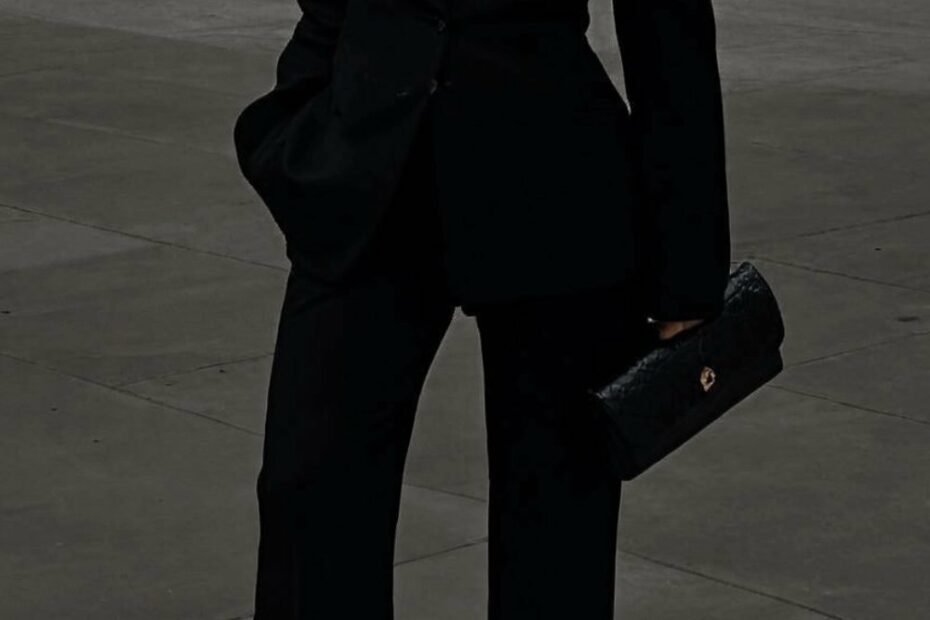 A person in a black suit exudes opulence outdoors, confidently holding a black clutch. Discover how to dress like a rich woman by embracing timeless elegance and sophisticated accessories.