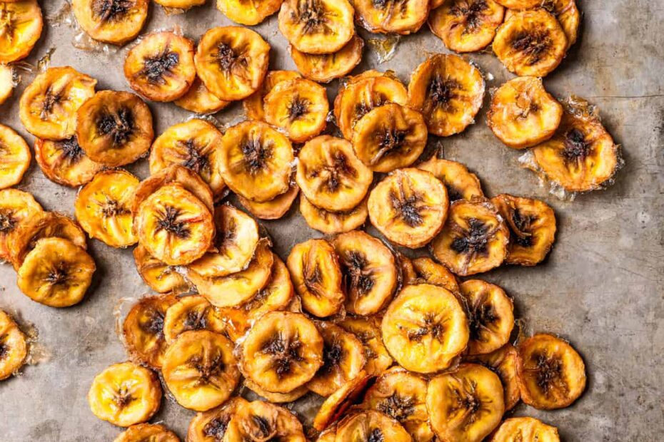 Overhead view of banana chips scattered over a grey surface.