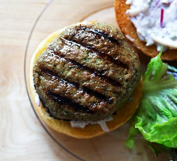 A plated turkey burger aside some lettuce, bun spread with raita.