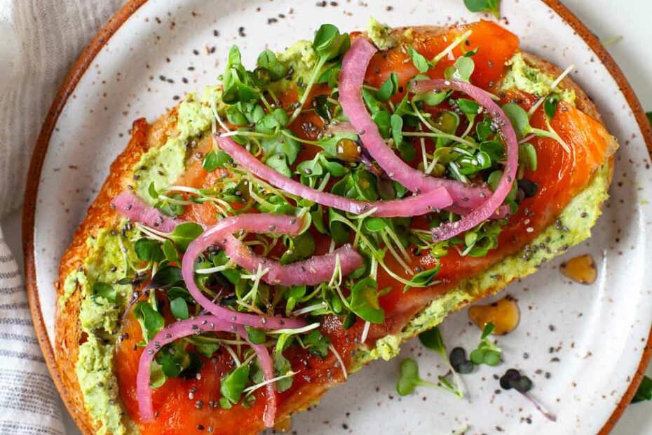smoked salmon toast with smashed edamame, pickled onions, honey, microgreens and chia on plate