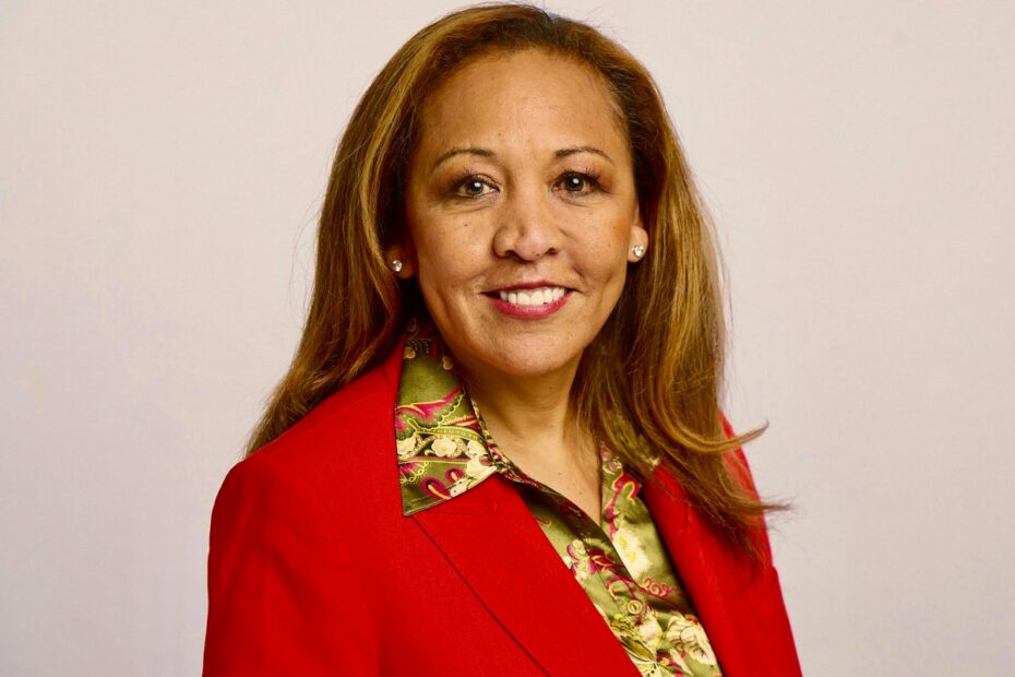 Woman with long hair in red jacket, smiling to camera.