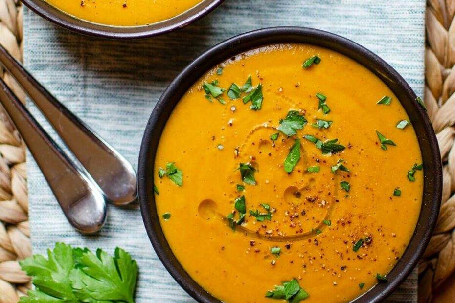 Closeup of two bowls of carrot lentil soup on a striped napkin.