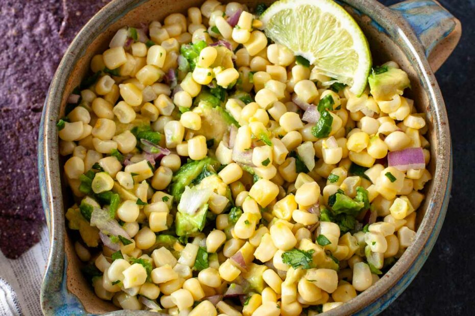 corn avocado salsa with lime wedge in brown and blue ceramic bowl next to blue tortilla chips