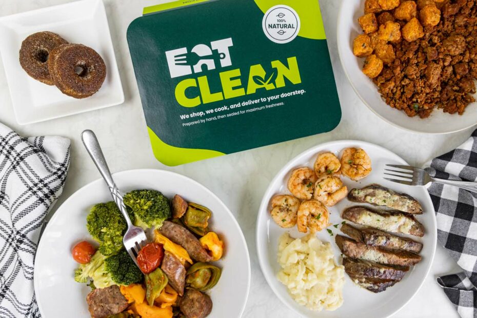 Overhead view of multiple Eat Clean meals arranged on a white marble surface. Visible dishes include pulled pork, sausage with vegetables, surf and turf with potatoes, meatballs, chicken nuggets with mac and cheese, and mini churro donuts. The plates feature different protein options, sides, and colorful vegetables, demonstrating the variety available in their meal plans.