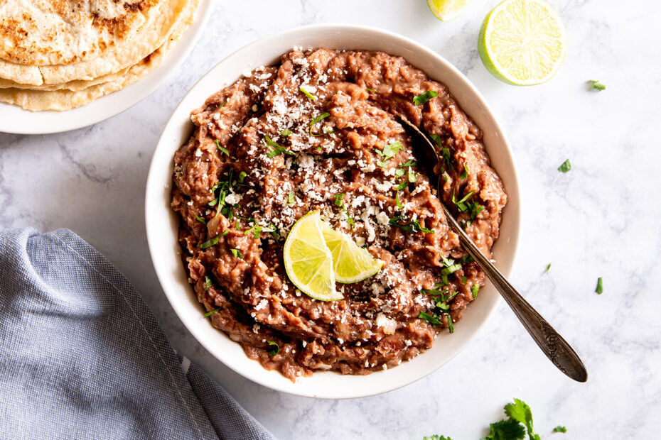 A bowl of refried beans topped with minced garlic, cilantro, and lime wedges.