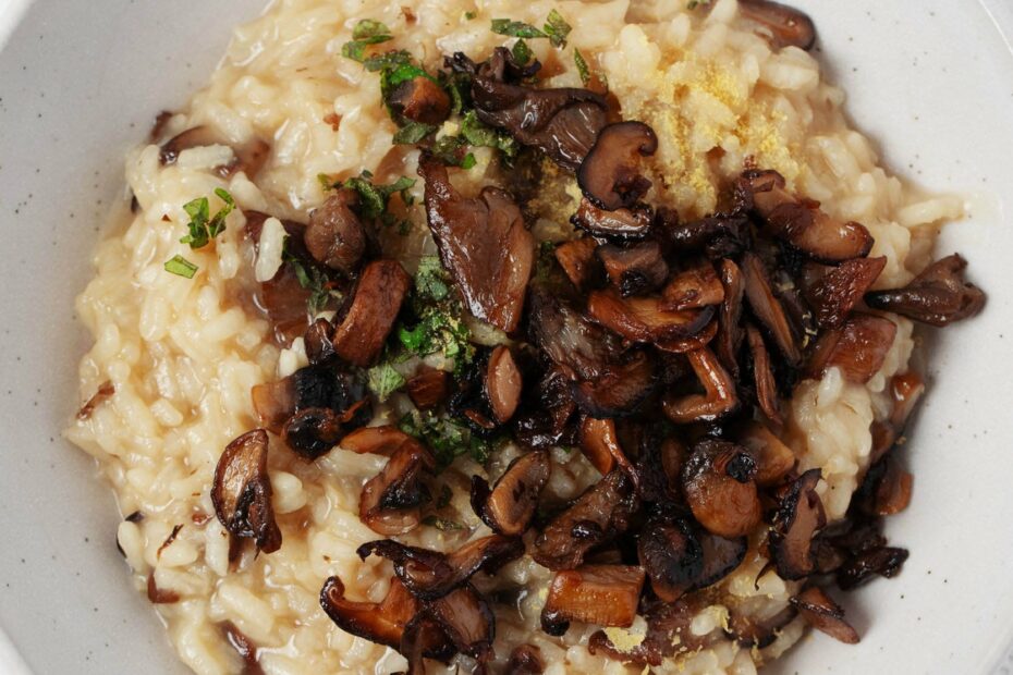 An overhead image of vegan mushroom risotto, which is garnished with green herbs and served in a white bowl.