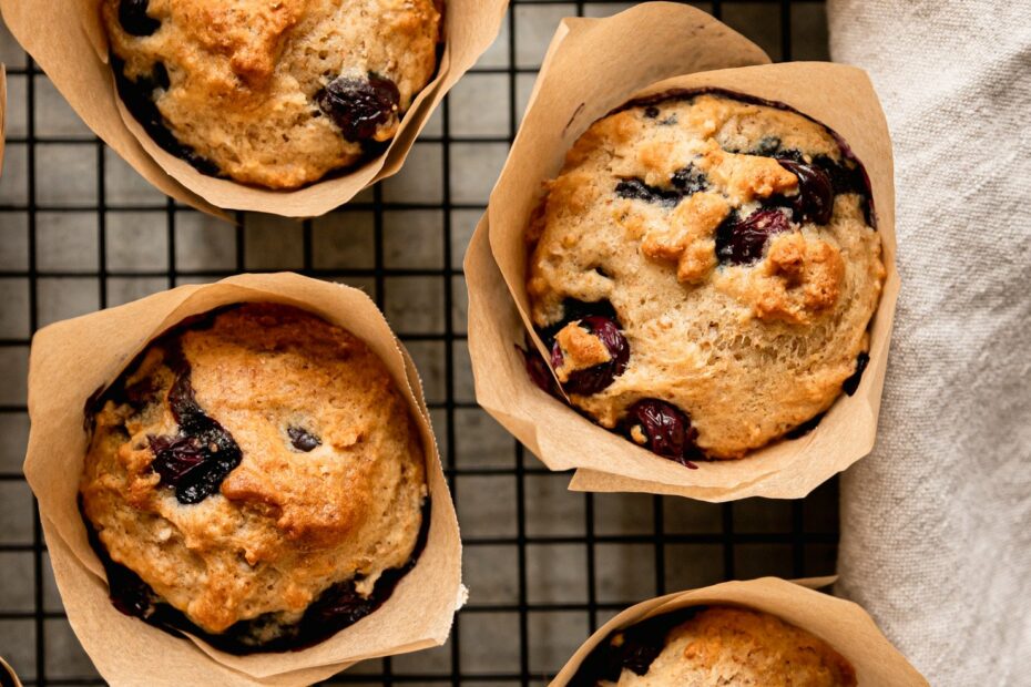 An overhead shot shows fluffy vegan blueberry muffins cooling on a wire rack. The muffins are in homemade parchment paper liners.