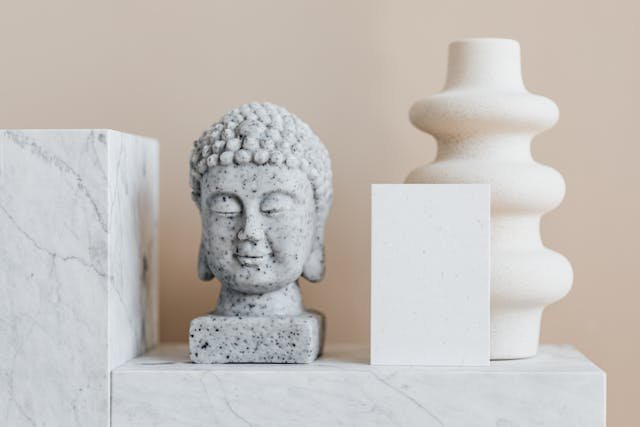 : Luxury interior design pieces featuring a marble Buddha sculpture, a modern white vase, and minimalist geometric blocks, all contributing to an elegant space