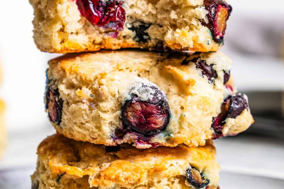 Three blueberry biscuits stacked on a plate with a bite missing from the top biscuit.