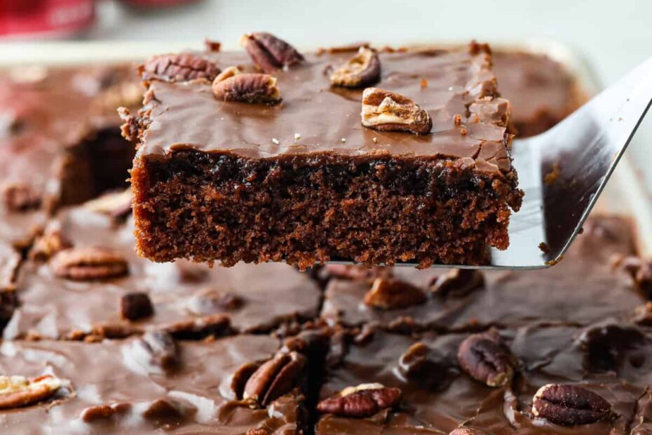 Side shot of someone lifting a slice of Dr. Pepper sheet cake out of the pan.