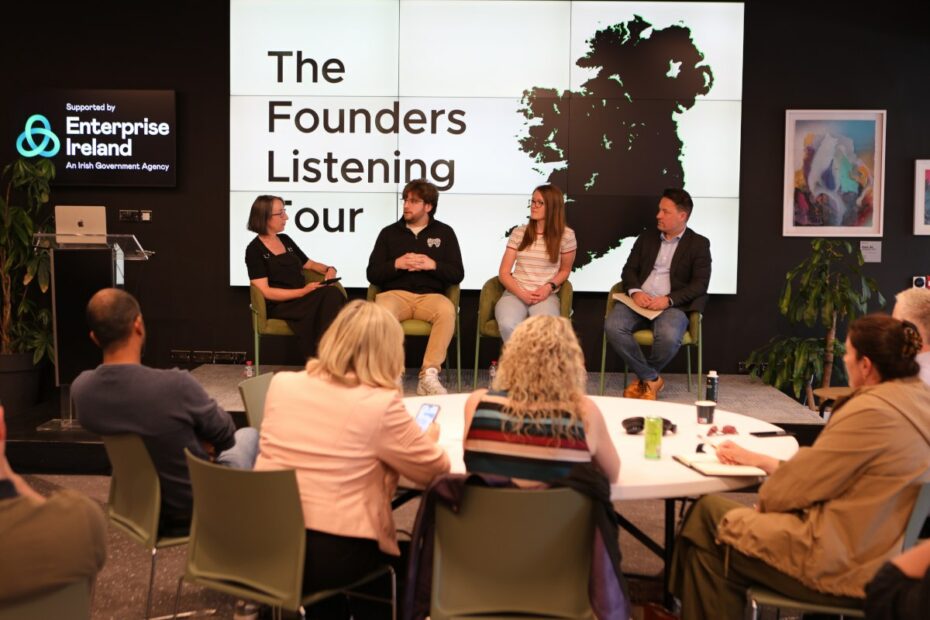 Backs of people's heads as they watch a panel discussion with two women and two men