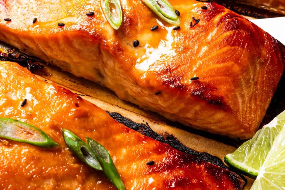 Close shot of miso salmon garnished with sesame seeds and scallions on a lined baking tray.