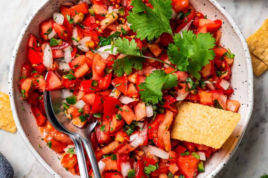 Overhead view of a tortilla chip resting in a bowl of pico de gallo.