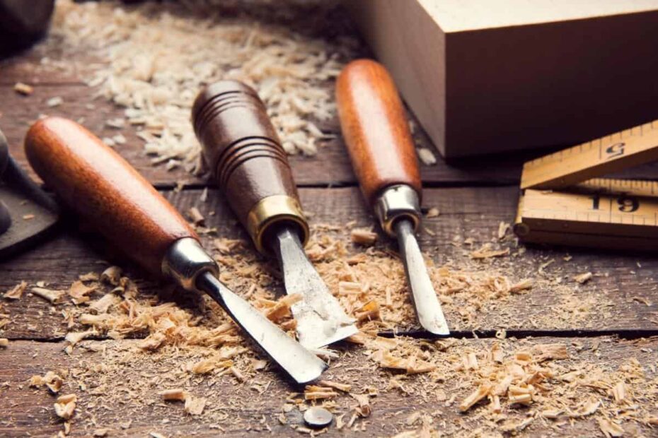 Three wood carving chisels rest on a wooden workbench, encircled by wood shavings and a ruler, ready to bring DIY woodworking projects to life.