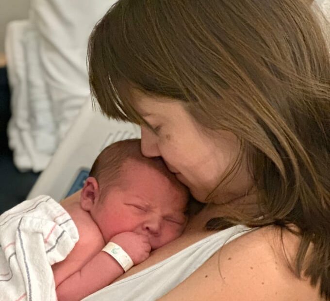 woman in hopsital bed with baby laying on her chest wrapped in a blanket