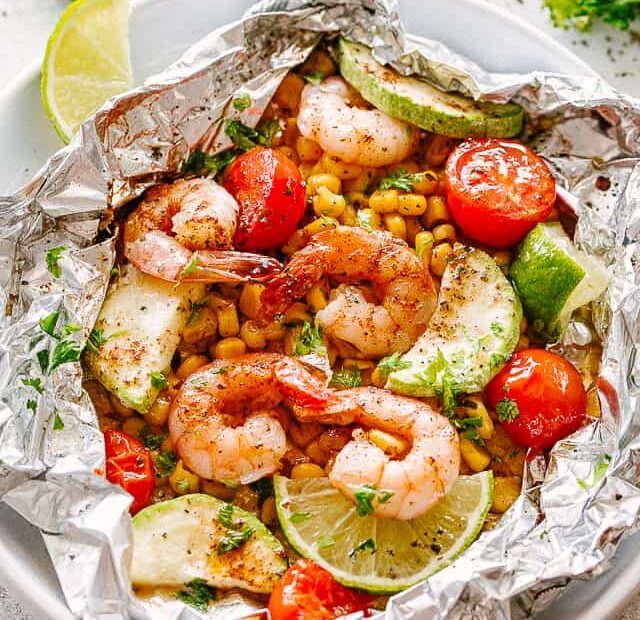 Overhead view of a grilled shrimp foil packet opened on a plate.