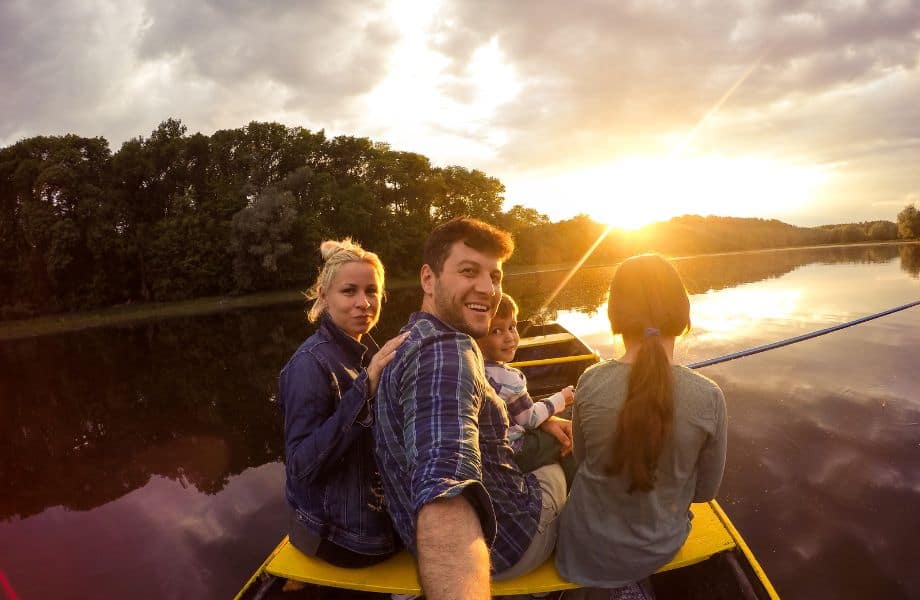 things to do in Wisconsin with kids, Selfie shot of a smiling family of four sitting in a rowing boat and fishing on a clear still lake with a row of trees behind and the bright setting sun on the horizon under a bank of clouds. where to stay in door county with kids