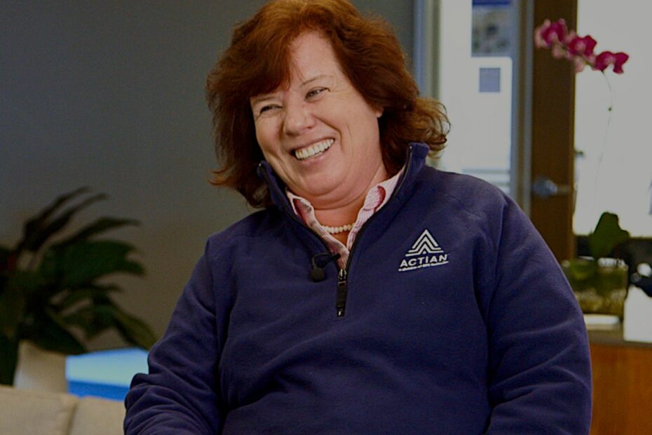 A woman with shoulder-length light brown hair smiles while wearing a navy fleece with the Actian logo on it.