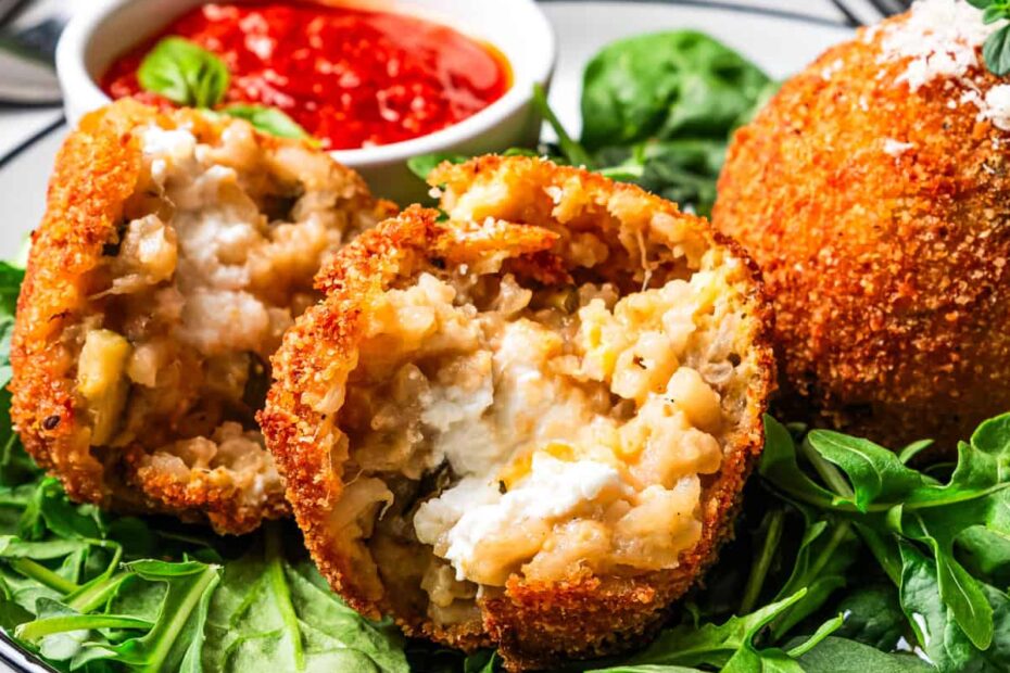 An arancini ball broken in half and served over a bed of greens on a plate.