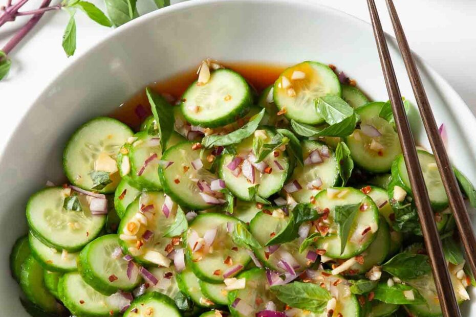 Overhead shot of Asian cucumber salad with chopped onions and herbs visible, and chopsticks on the side.