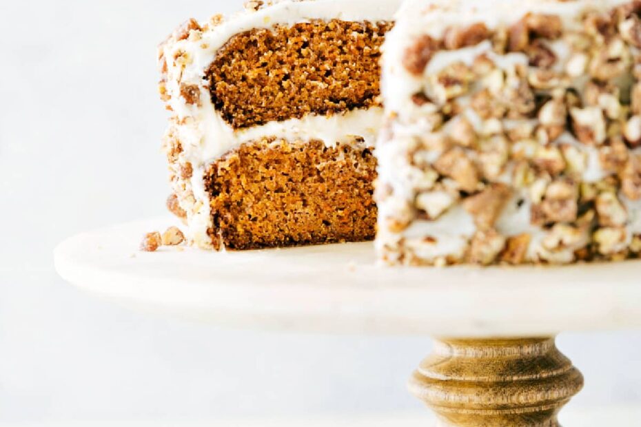 This carrot cake rests on a cake stand with a large slice removed, revealing its rich, layered interior.