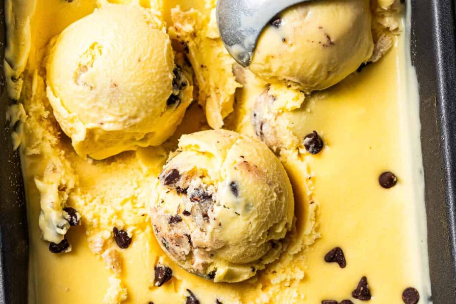 An ice cream scoop resting in a tub of chocolate chip cookie dough ice cream.