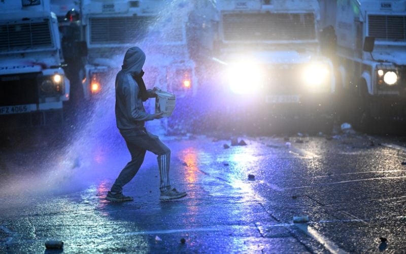 June 11, 2025:  A member of the crowd throws an object towards the PSNI riot squad officers as they form a blockade near Harryville bridge to stop potential rioters from accessing the Clonavon terrace area in Ballymena, Co Antrim.