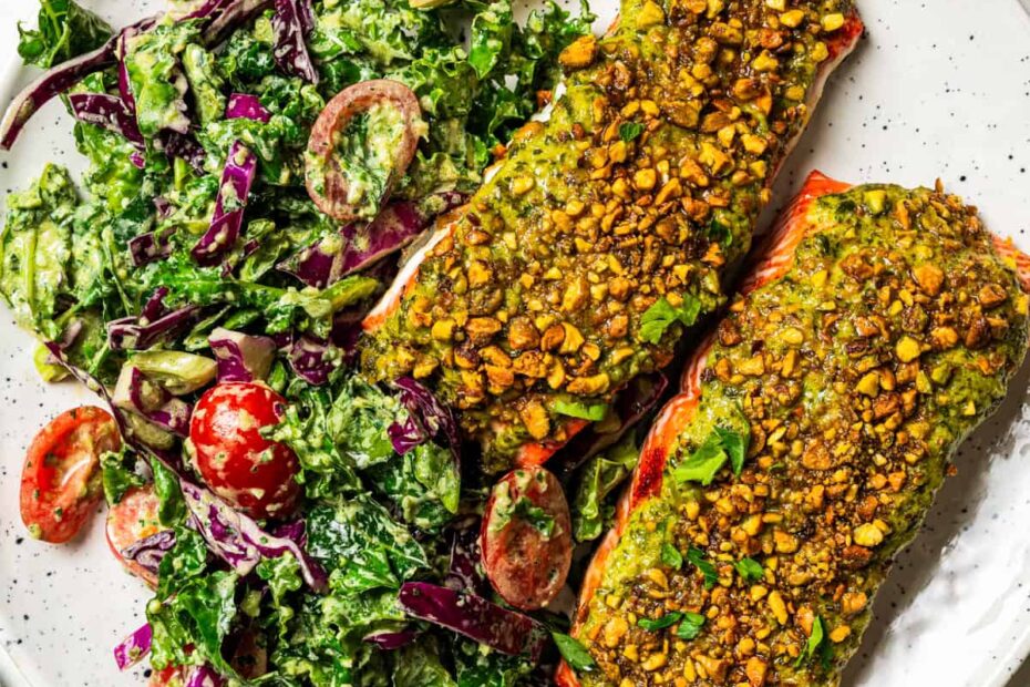 Two pistachio crusted salmon filets with a side of kale salad on a plate.