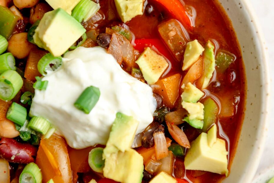 Bowl of three bean chili topped with sour cream, avocado and green onions.