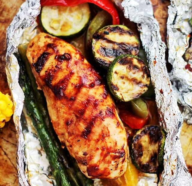 Overhead view of a grilled chicken foil pack open to reveal the BBQ chicken with veggies.