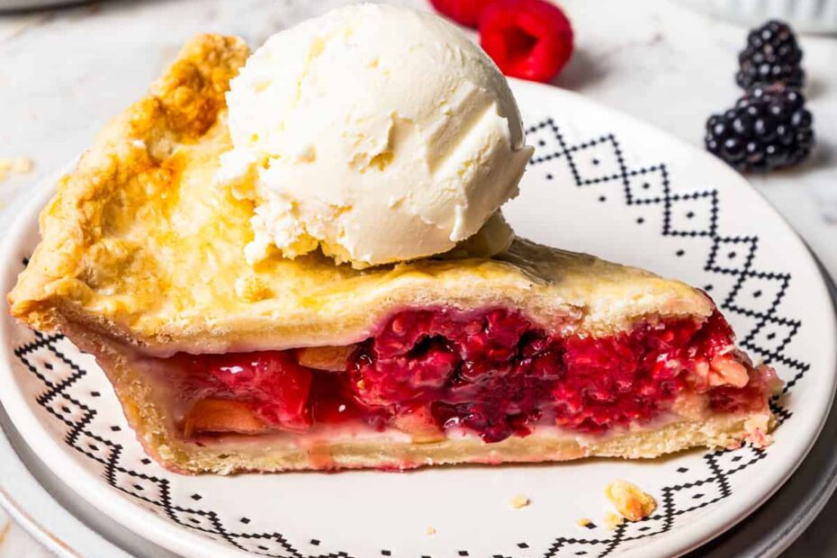 A slice of berry pie topped with a scoop of ice cream on a plate.
