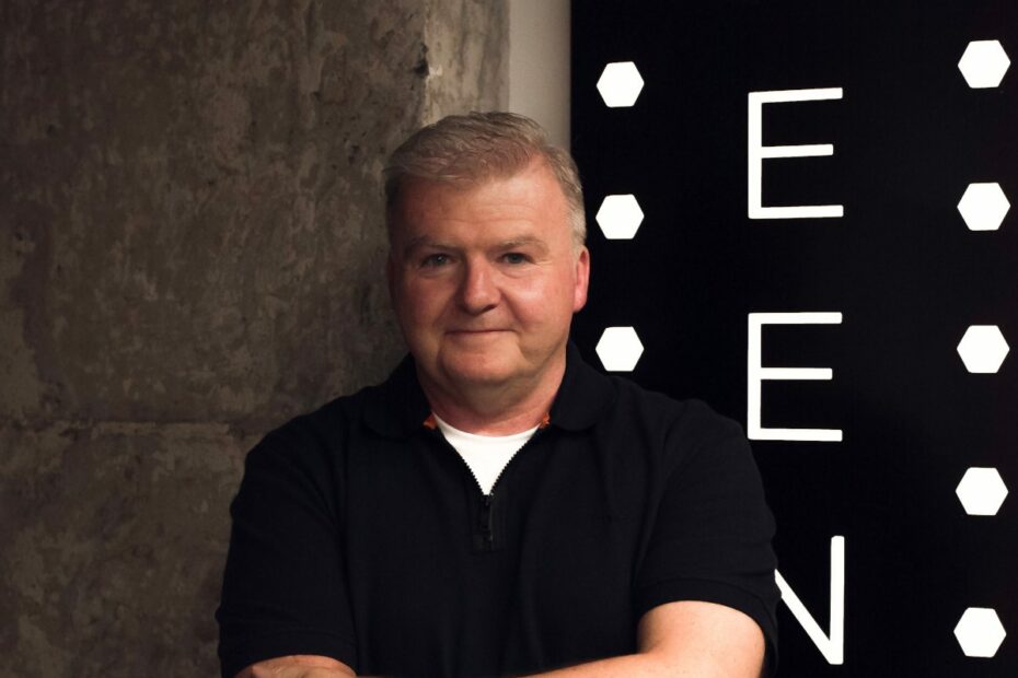 Donal McGuiness stands in a black t-shirt with his arms folded.