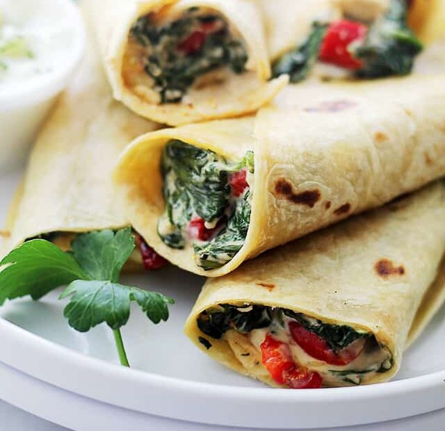 Assorted spinach feta wraps stacked on a white plate.