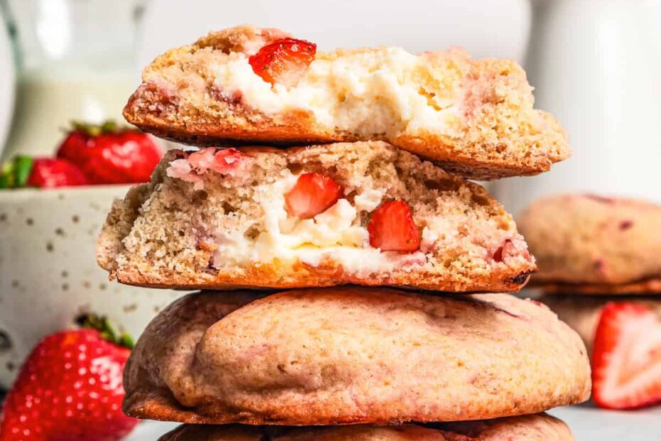 Four strawberry cheesecake cookies stacked on a plate with a bite missing from the top two cookies.