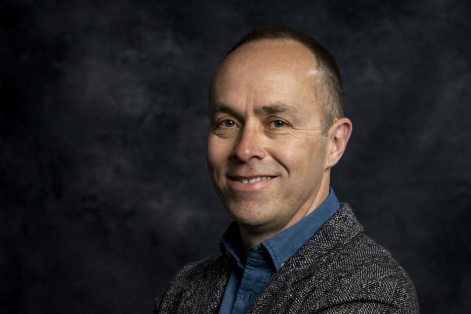 Headshot of John Garvey wearing a grey suit in a dark room.