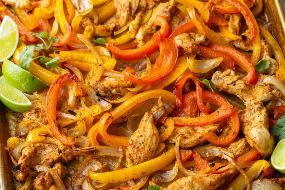 sheet pan chicken fajitas cooked on a cookie sheet with chicken, red and yellow peppers, onions and lime wedges