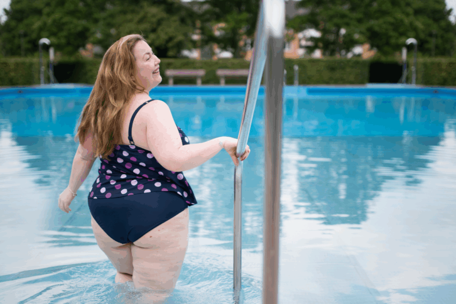 Young plus-size woman in a polka-dotted bathing suit stepping into a pool while smiling