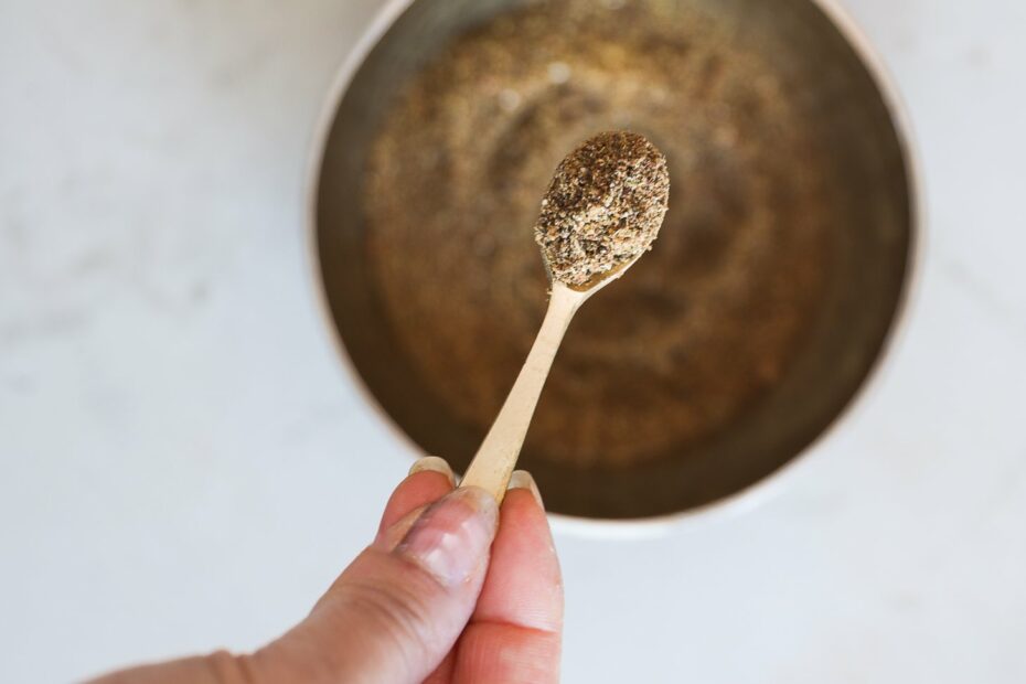 A hand holds a small spoon of freshly ground chai masala over a bowl.